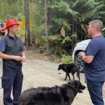 Two men talk while two dogs mill about before going on a walk to see a forest project